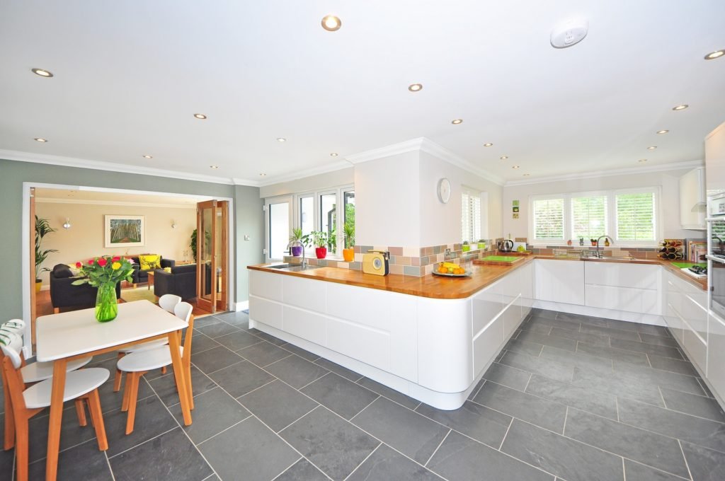 Bright open-plan kitchen with white cabinets, wooden countertops, and a dining table; living room visible through the doorway to the left.