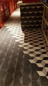 Black-and-white geometric tile floor with a 3D cube pattern beside a tiled counter in a dimly lit space.