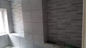 Grey tiled bathroom under construction with a window sill and recessed wall niche near the corner
