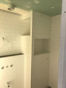 Under-construction shower with white subway tiles, built-in recessed niches, and exposed plumbing fittings on the left wall