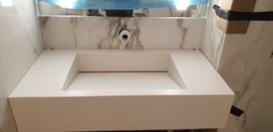 White bathroom vanity with a rectangular sink opening, marble walls, and an exposed drain hole in a bathroom under installation.