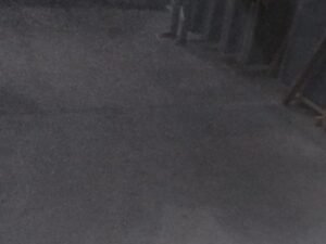 Dark indoor floor, likely concrete, with faint dust and vertical wooden supports along the right edge