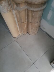 Old brown clay sewer/vent pipes arranged in a corner against a plaster wall, resting on light gray tiled floor.