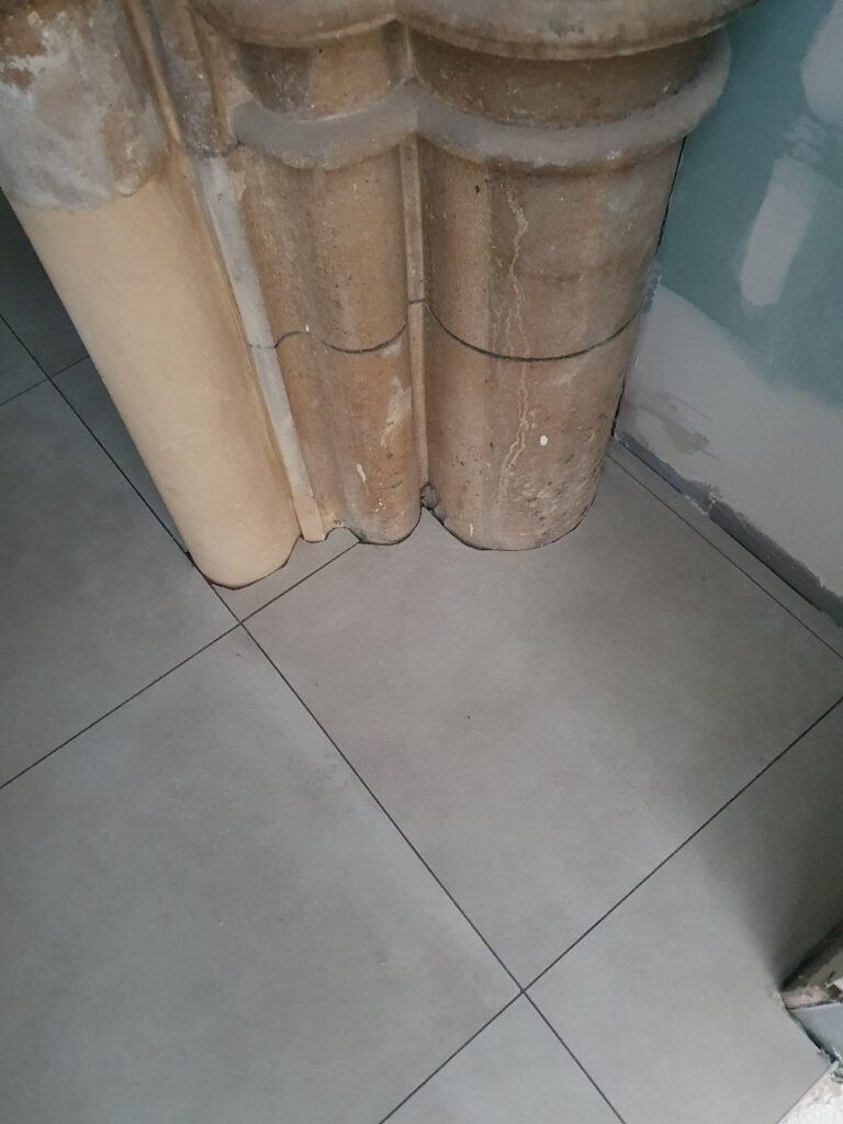 Old, dusty brown ceramic columns or sculpted pillars standing on a tiled floor by a wall; they appear cracked and weathered.