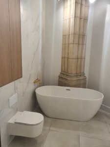 Modern bathroom with a freestanding white tub beside a large stone column and marble wall panels.